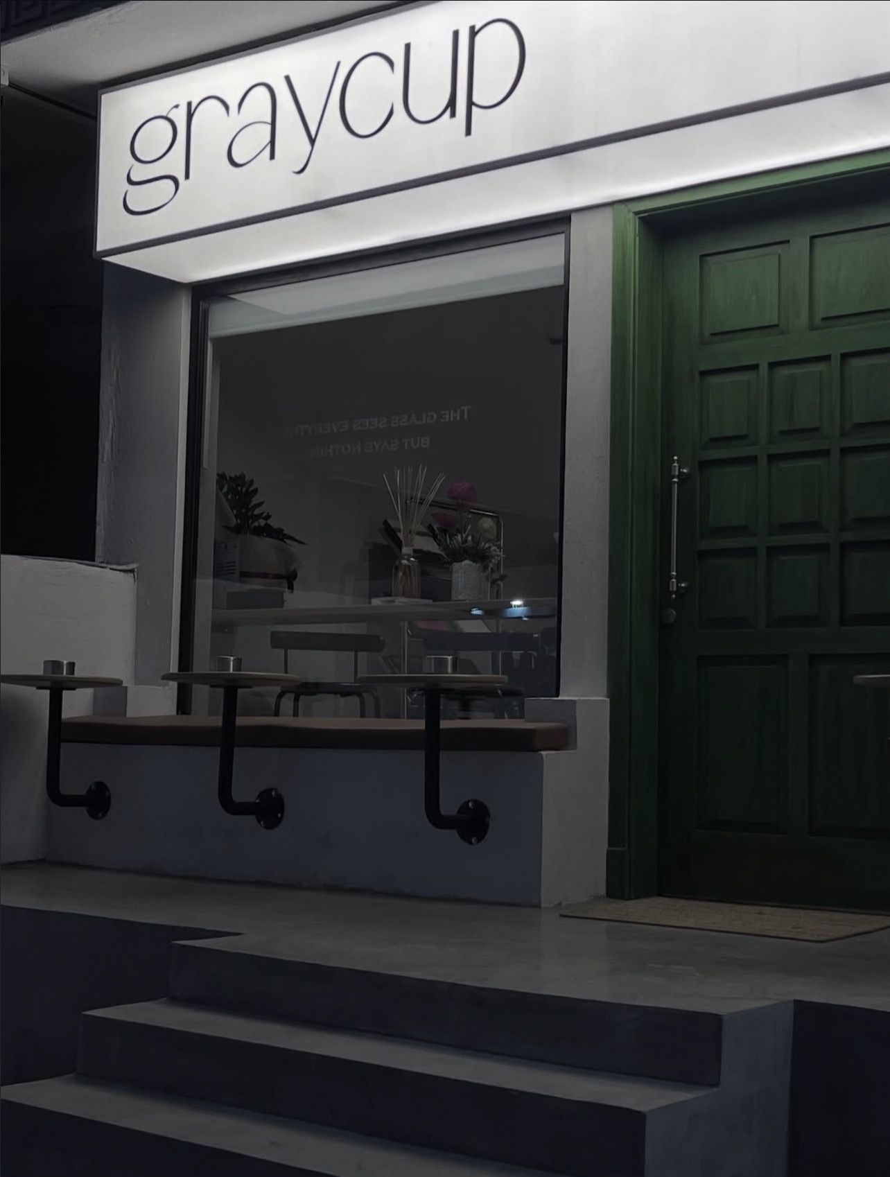 واجهة graycup المضيئة ليلًا وبابها الأخضر